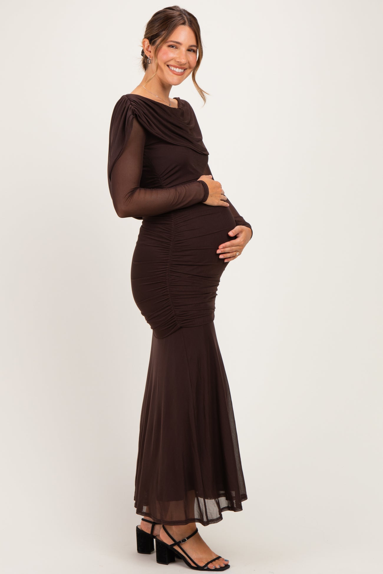 woman wearing a long sleeve brown maternity gown with ruching and a flared skirt, holding her baby bump