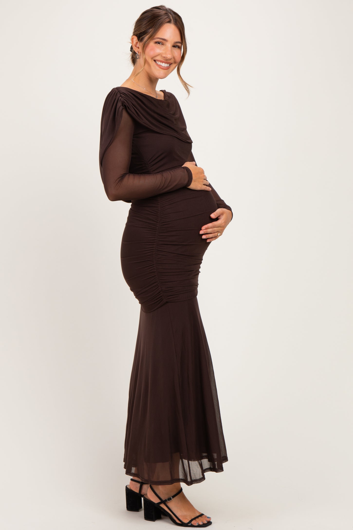 woman wearing a long sleeve brown maternity gown with ruching and a flared skirt, holding her baby bump