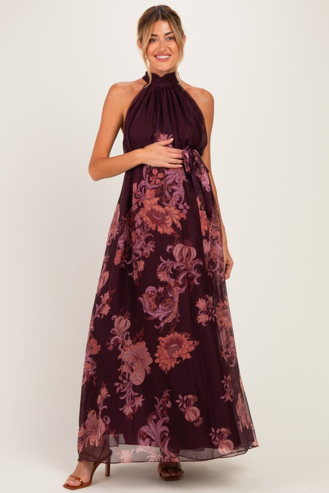 woman wearing a burgundy floral halter neck maternity maxi dress and holding her baby bump
