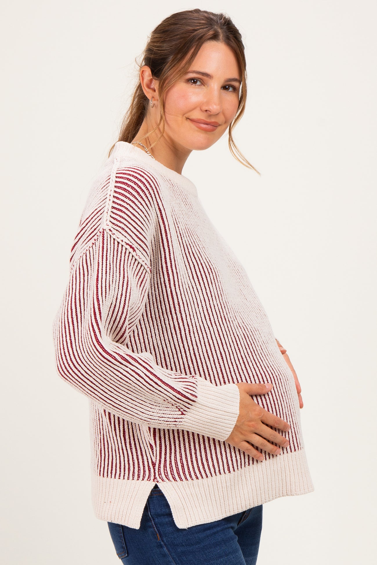 woman wearing a cream and red striped maternity sweater, smiling and gently holding her baby bump