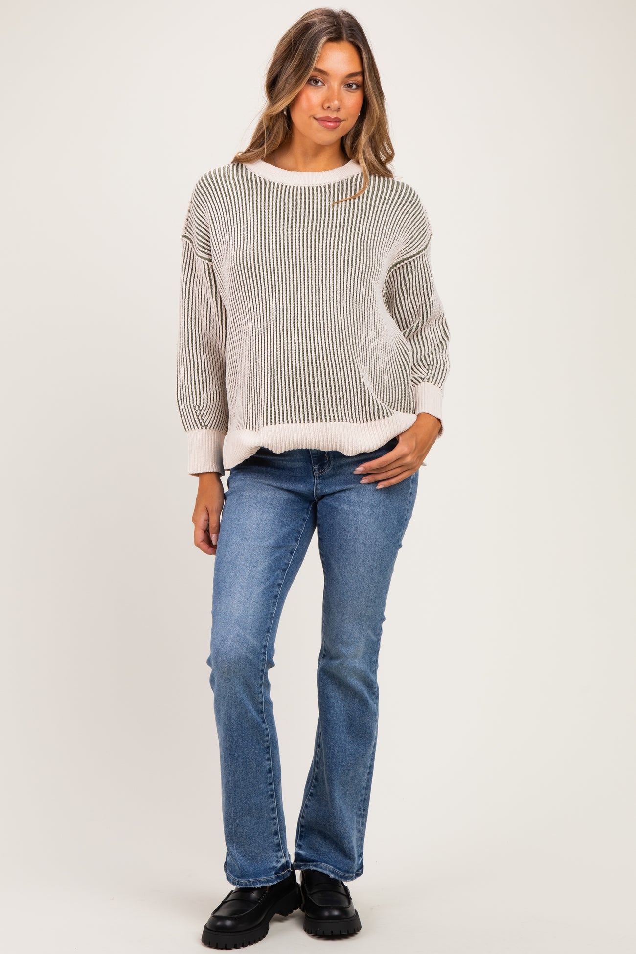 woman wearing a striped cream and gray maternity sweater with loose sleeves and blue maternity jeans