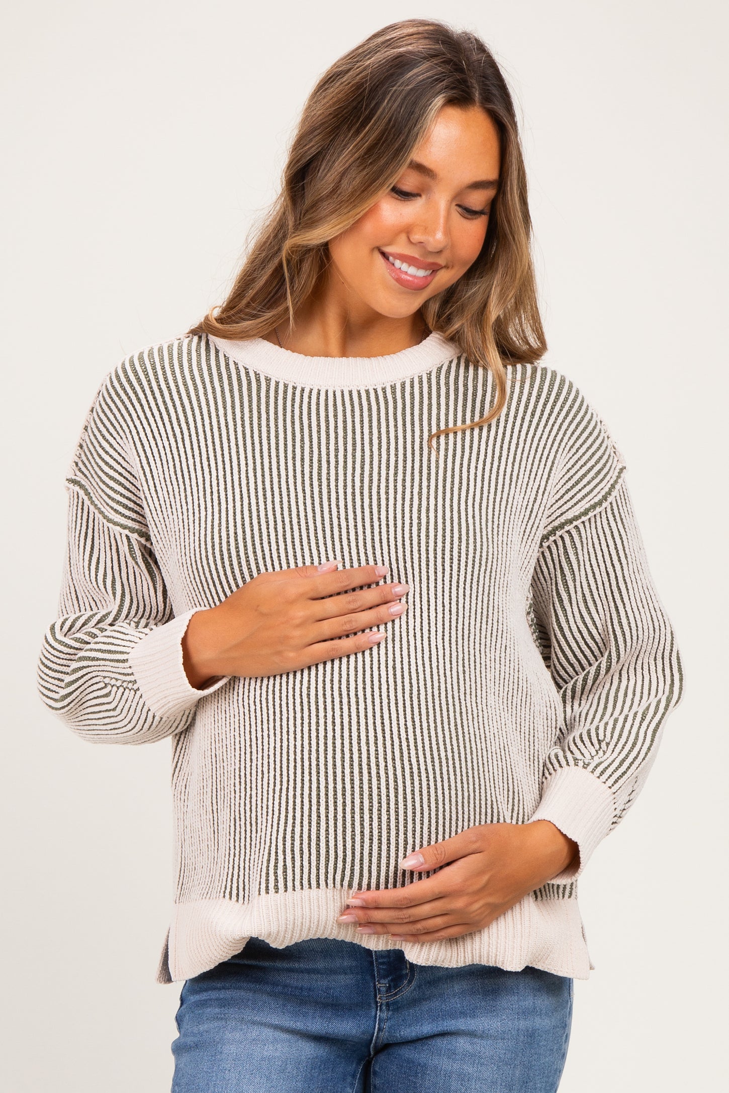 woman wearing a striped maternity sweater in neutral tones and holding her baby bump