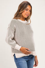 woman wearing a striped beige and grey maternity sweater and holding her baby bump