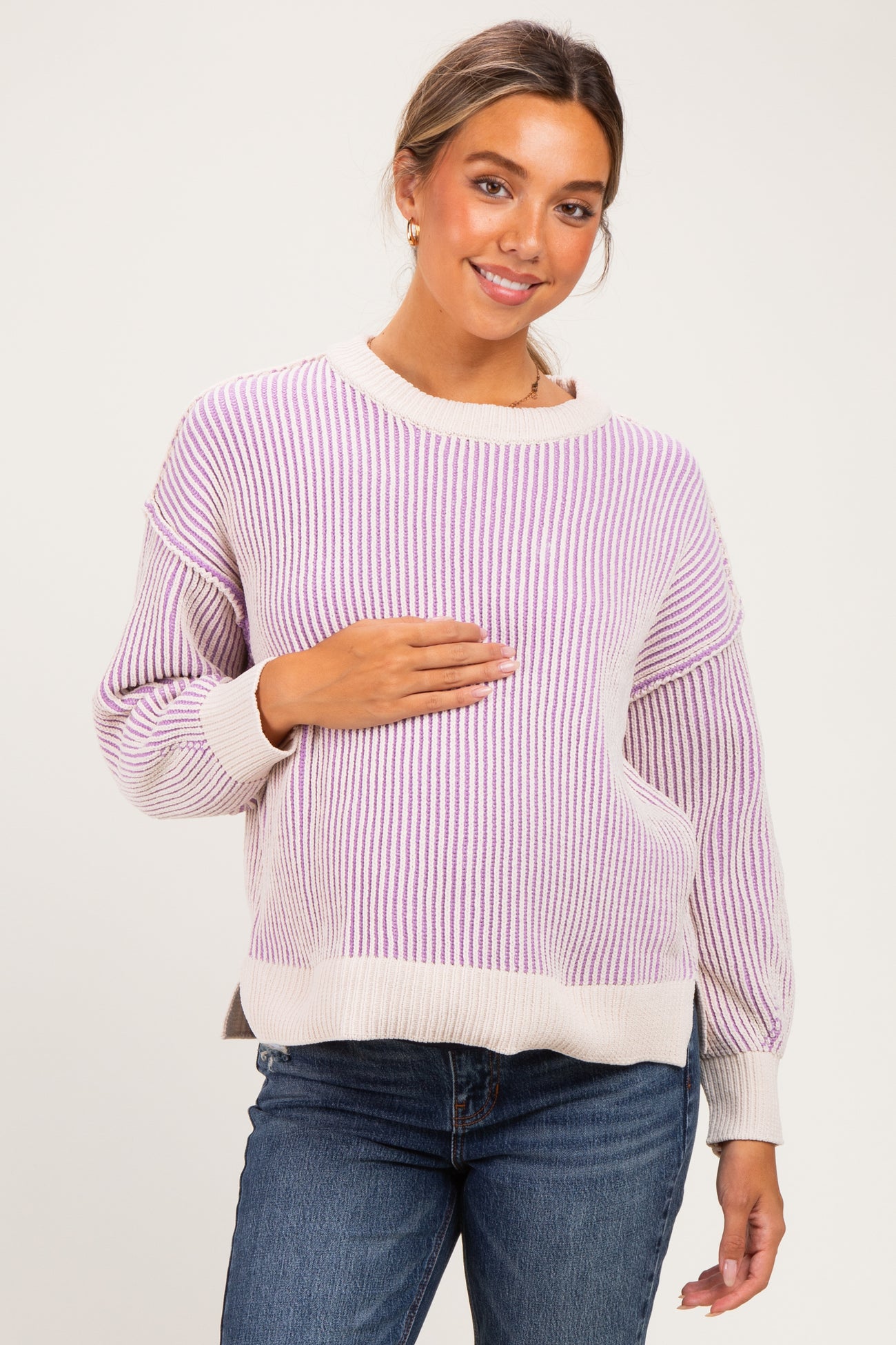 woman wearing a light purple and cream striped maternity sweater and holding her baby bump