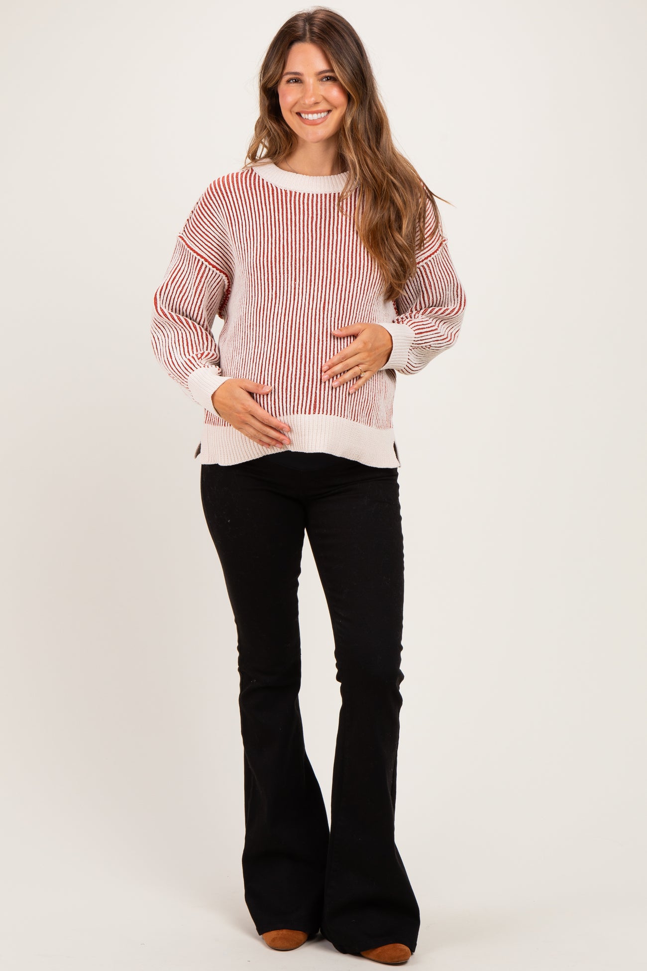 woman wearing a red and white striped maternity sweater and holding her baby bump, paired with black flared pants