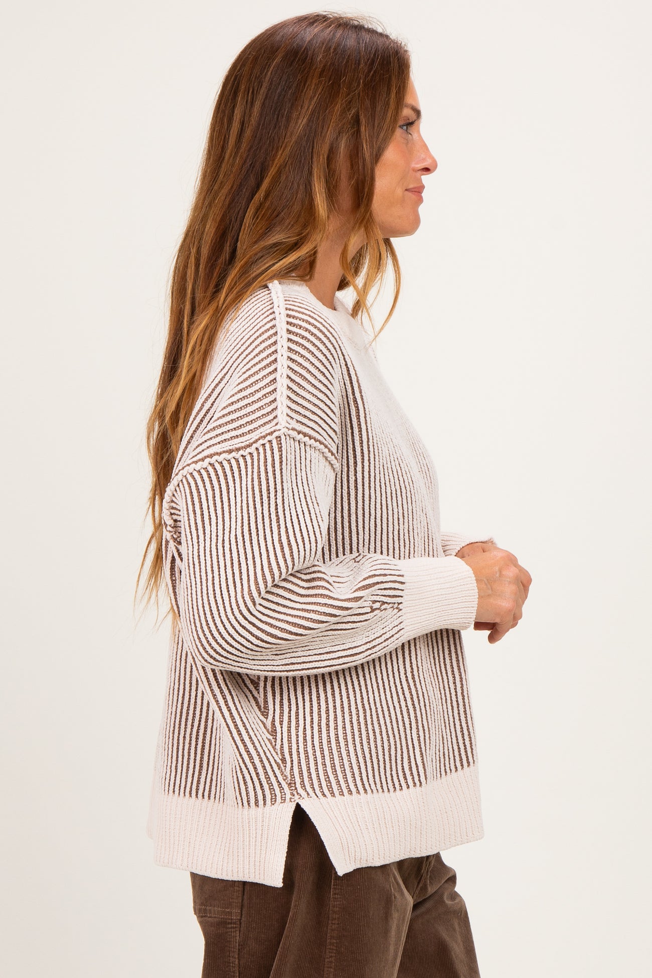 woman wearing a beige and brown striped oversized sweater with side slits and long sleeves