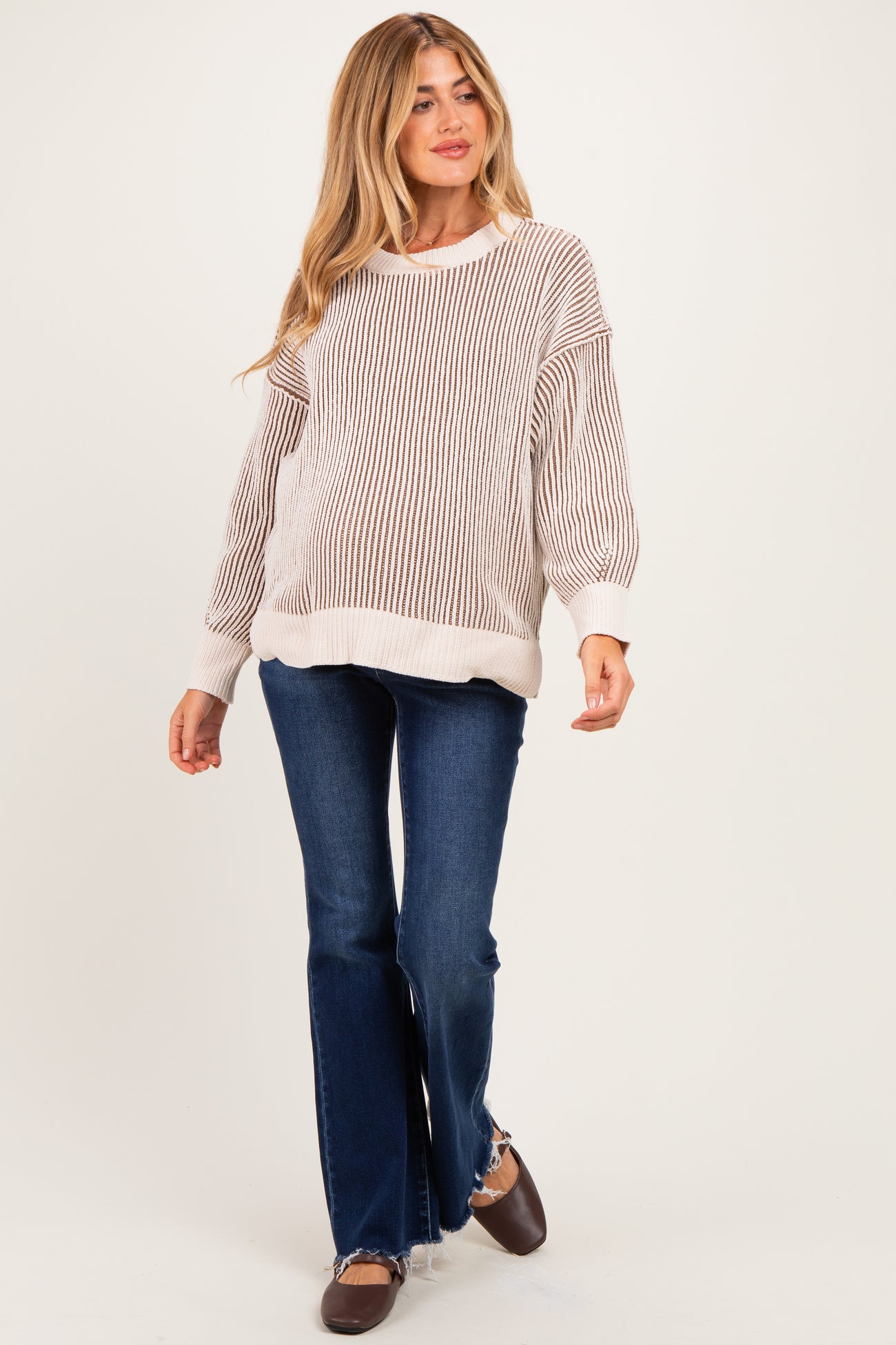 woman wearing a light striped maternity sweater with wide cuffs and bell-bottom jeans, walking confidently
