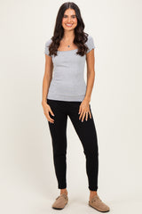 woman wearing a gray short sleeve fitted top and black jogger pants, standing with a smile