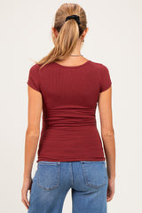 woman wearing a maroon fitted maternity top with short sleeves, seen from the back, paired with blue jeans