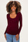 woman wearing a burgundy long sleeve maternity top with a scoop neckline and showing her baby bump