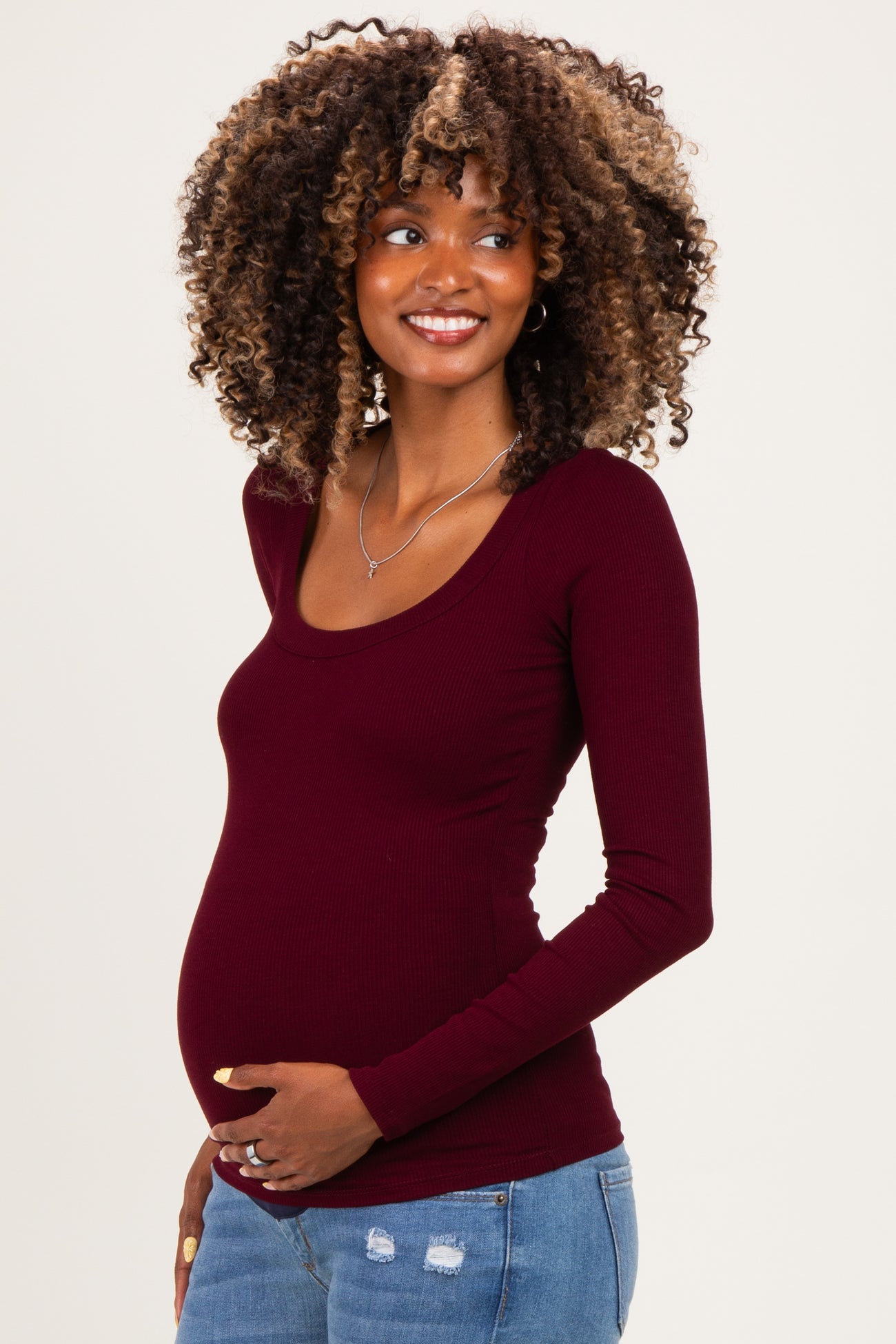 woman wearing a burgundy long sleeve maternity top and holding her baby bump