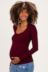 woman wearing a burgundy long sleeve maternity top and holding her baby bump