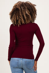 woman wearing a burgundy long sleeve maternity top, showing the back view, paired with blue jeans