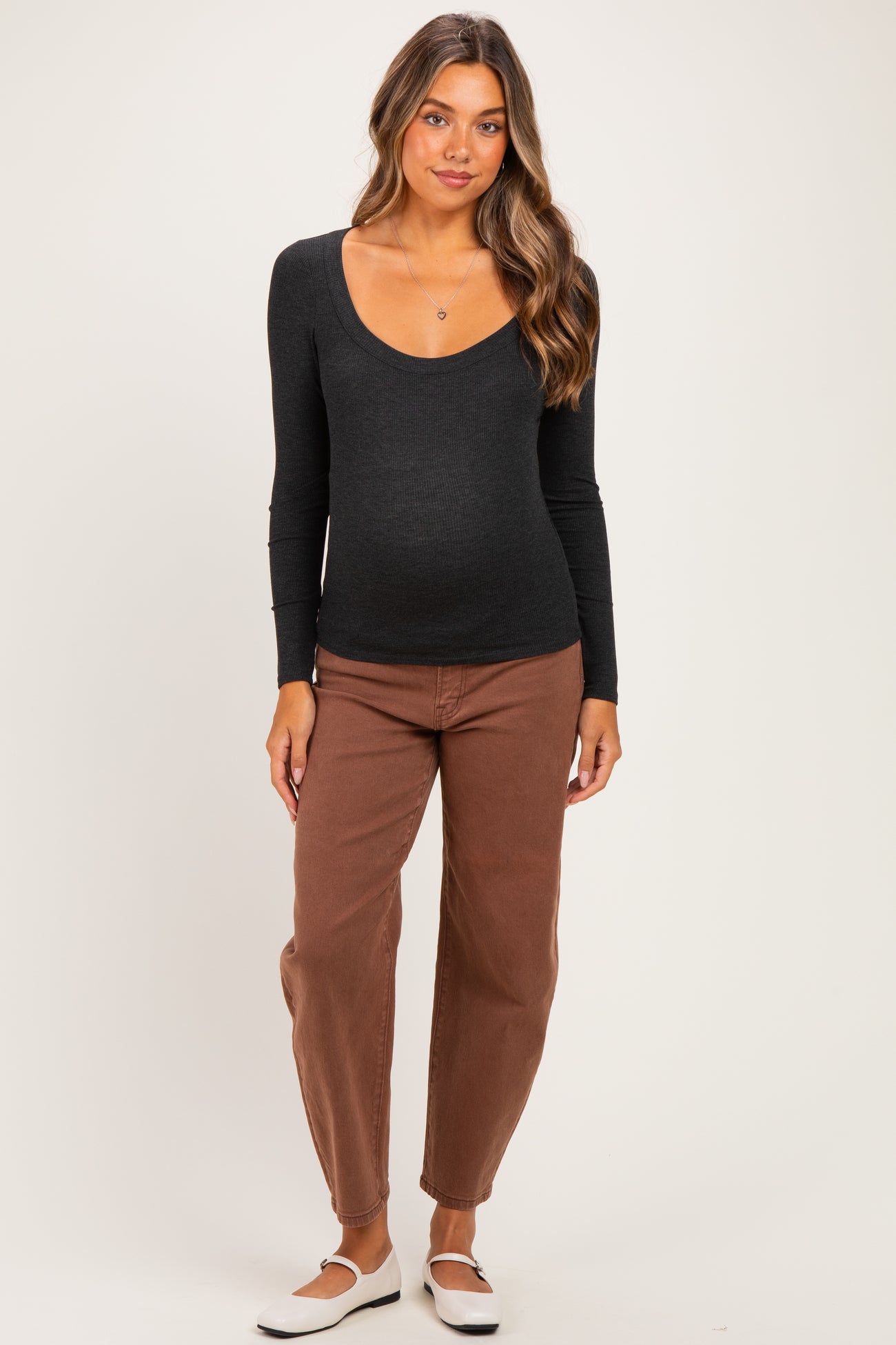 woman wearing a black long sleeve maternity top and brown pants, showing a visible baby bump