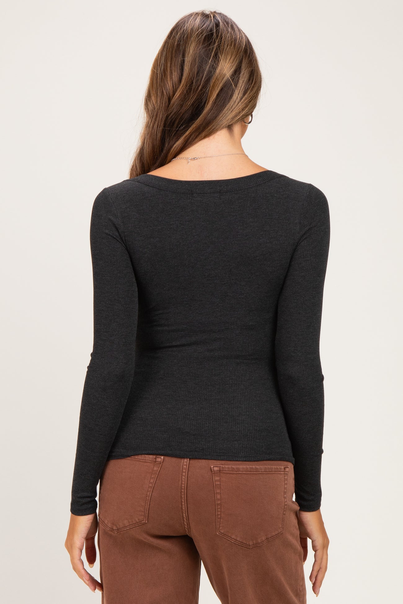 woman wearing a black long sleeve maternity top, viewed from the back, paired with brown pants