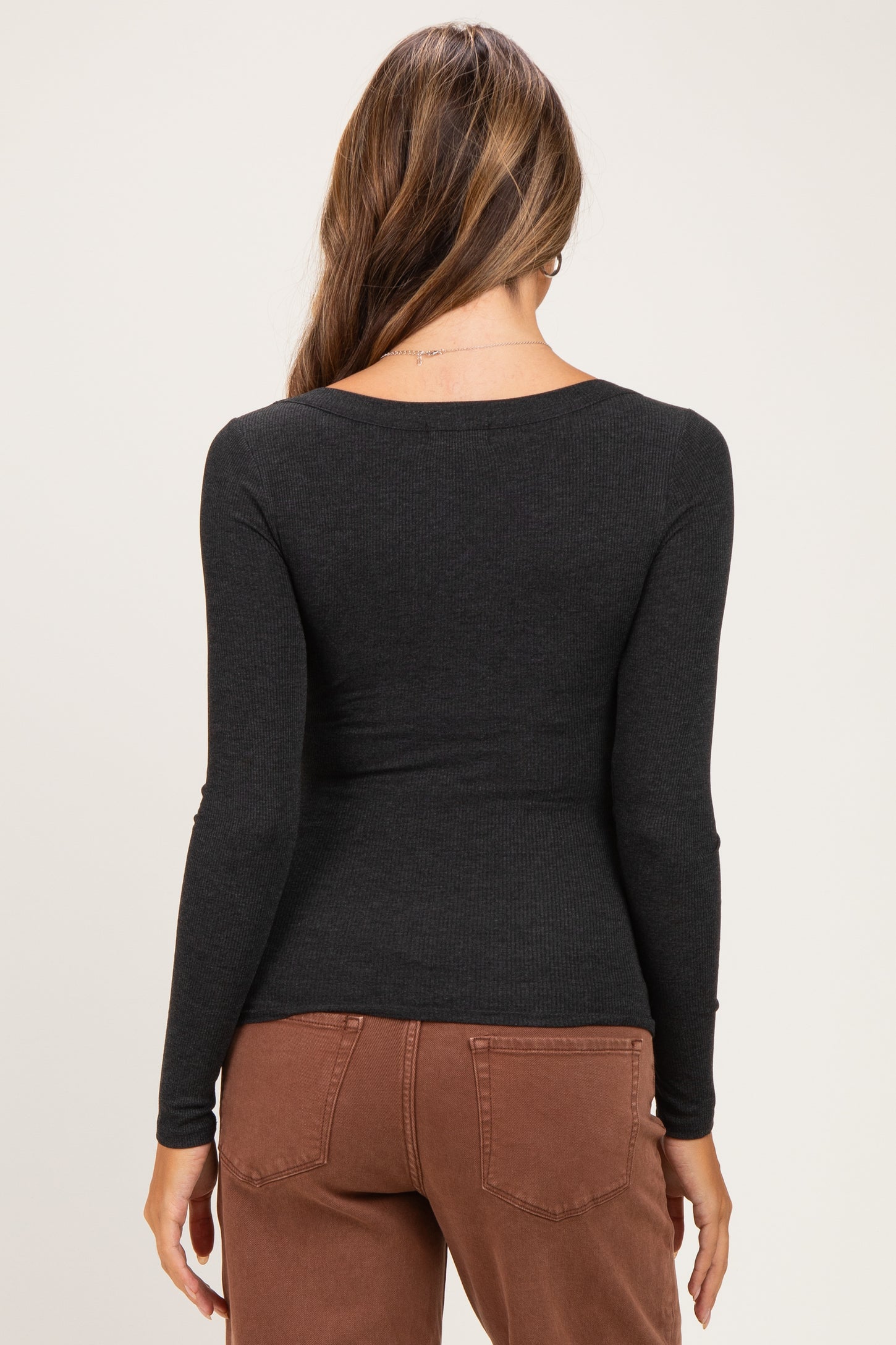 woman wearing a black long sleeve maternity top, viewed from the back, paired with brown pants