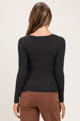 woman wearing a black long sleeve maternity top, viewed from the back, paired with brown pants