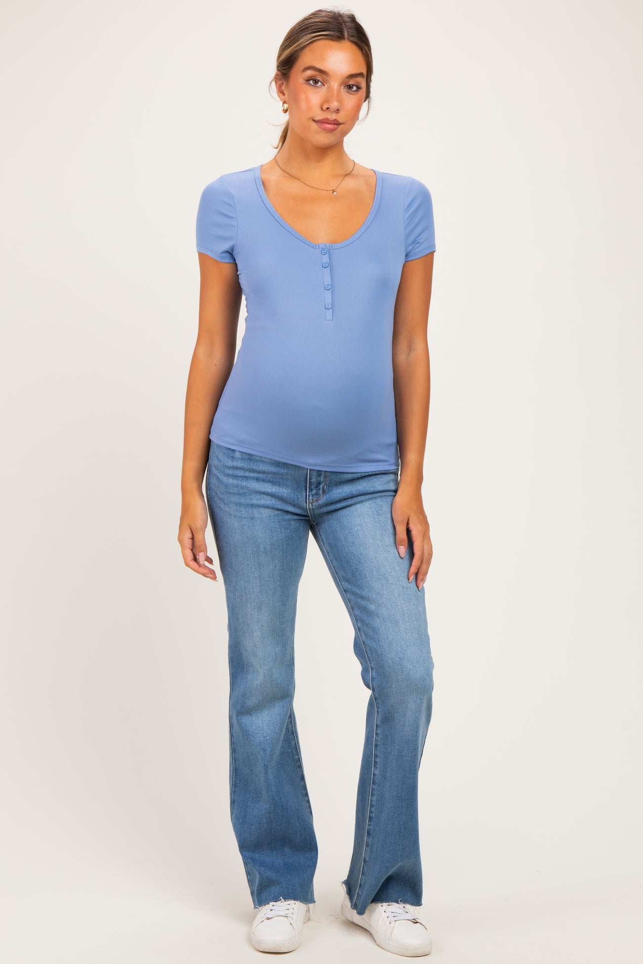 woman wearing a light blue maternity top with short sleeves and a scoop neckline, paired with flare jeans and showing her baby bump