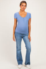 woman wearing a light blue maternity top with short sleeves and a scoop neckline, paired with flare jeans and showing her baby bump