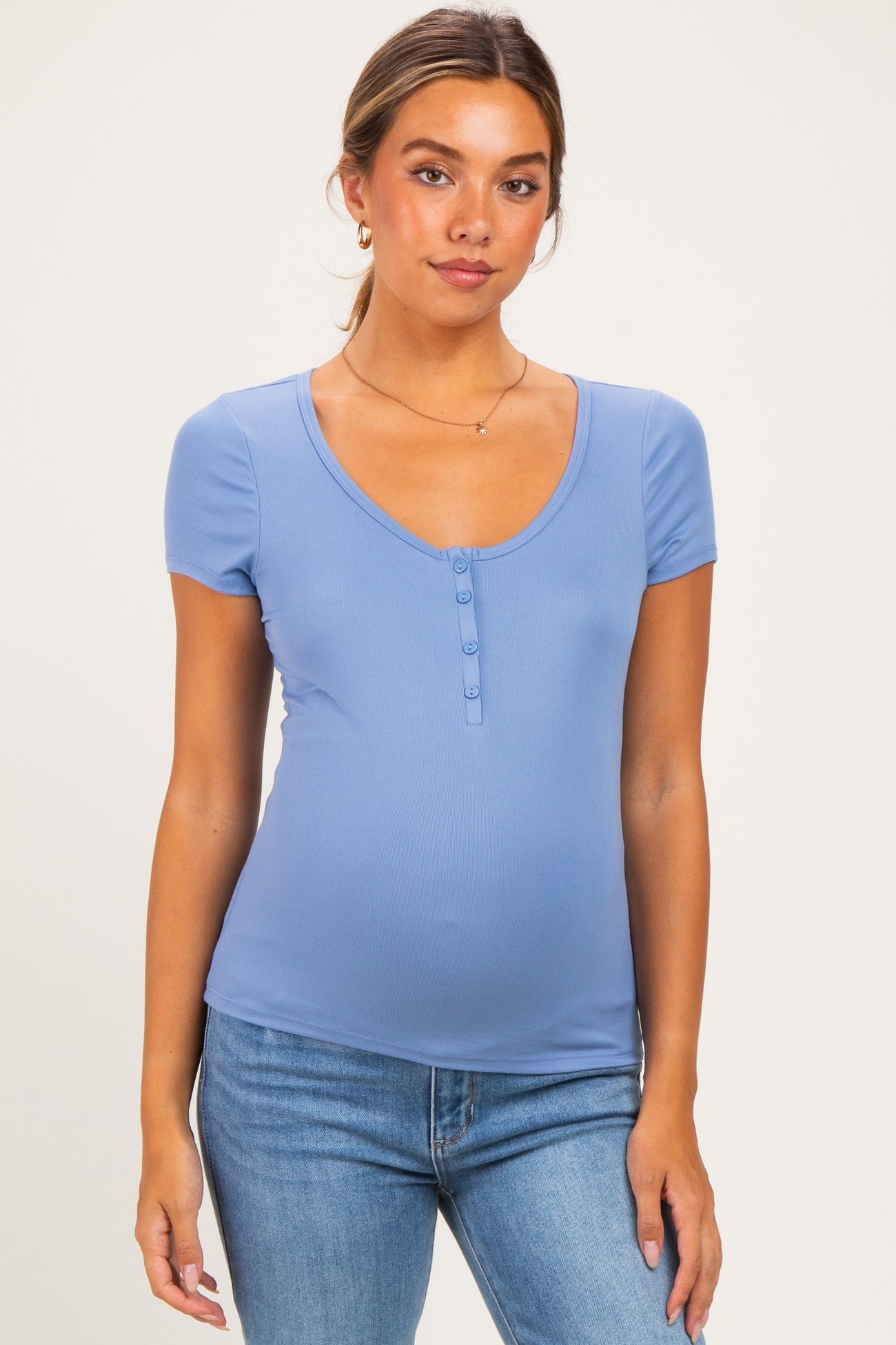 woman wearing a light blue maternity top with short sleeves and button detail, showing her baby bump