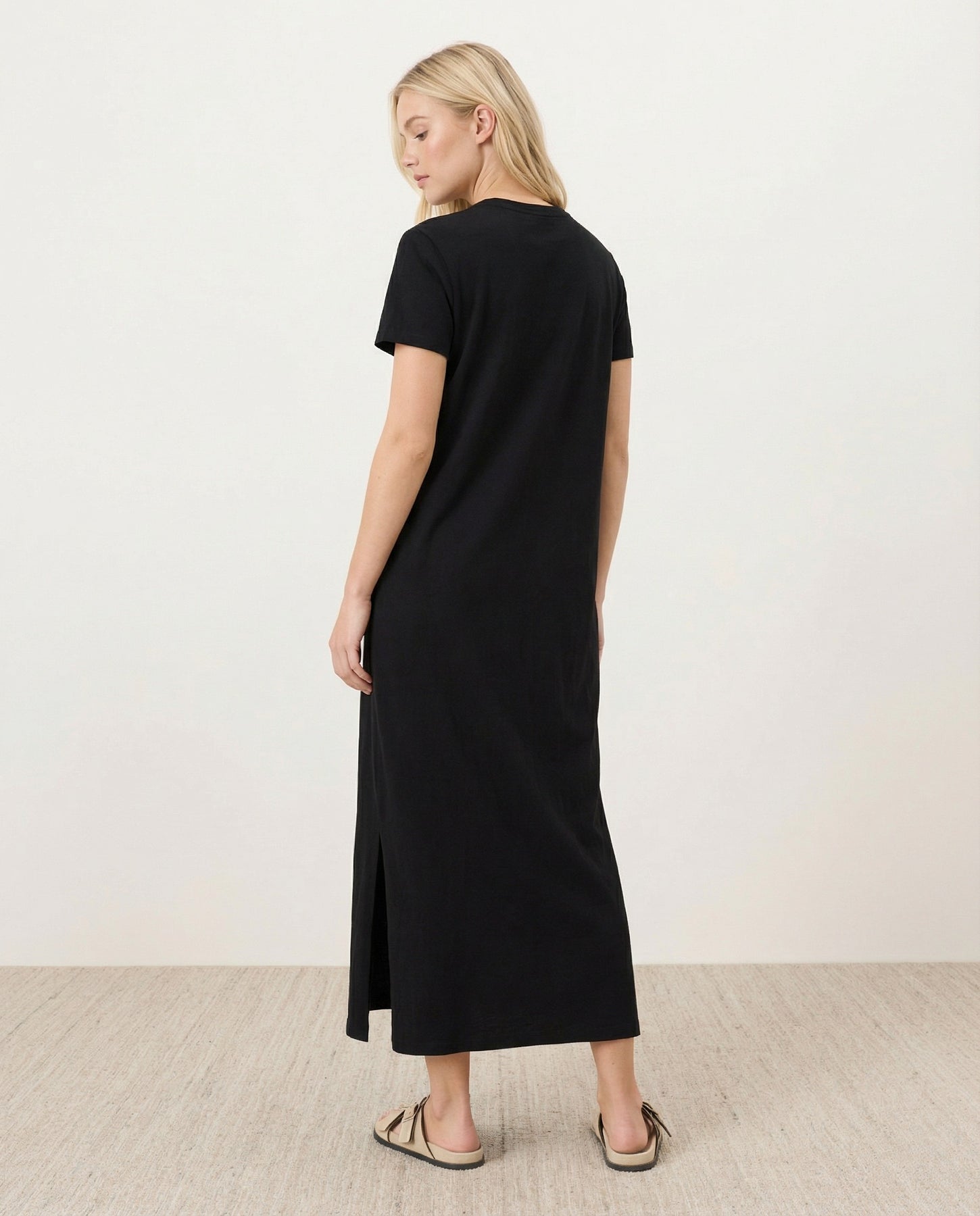 woman wearing a black short sleeve maxi dress with a side slit, viewed from the back