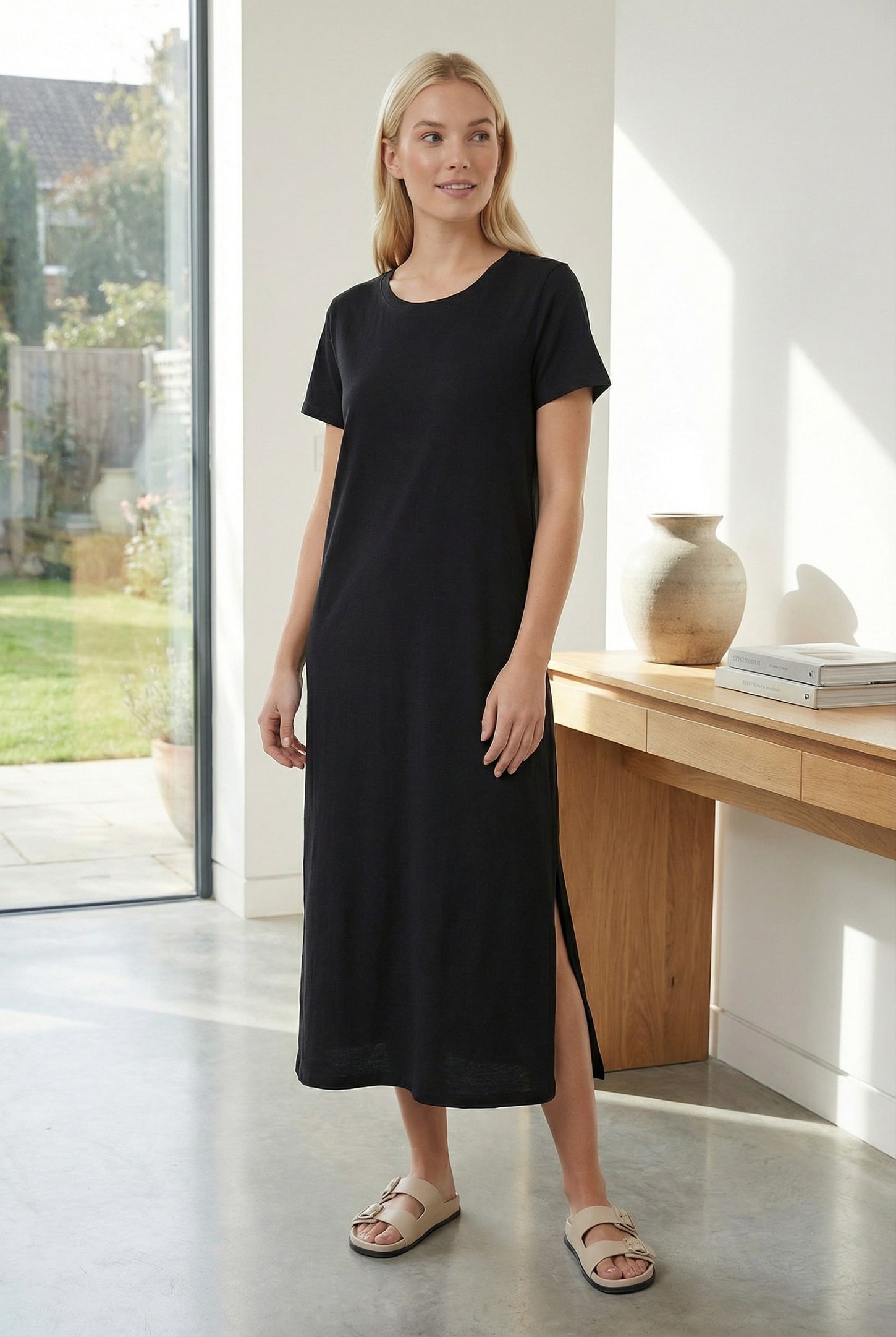 woman wearing a black short sleeve maxi dress with a side slit and casual sandals, standing indoors