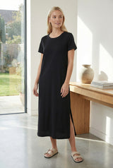woman wearing a black short sleeve maxi dress with a side slit and casual sandals, standing indoors