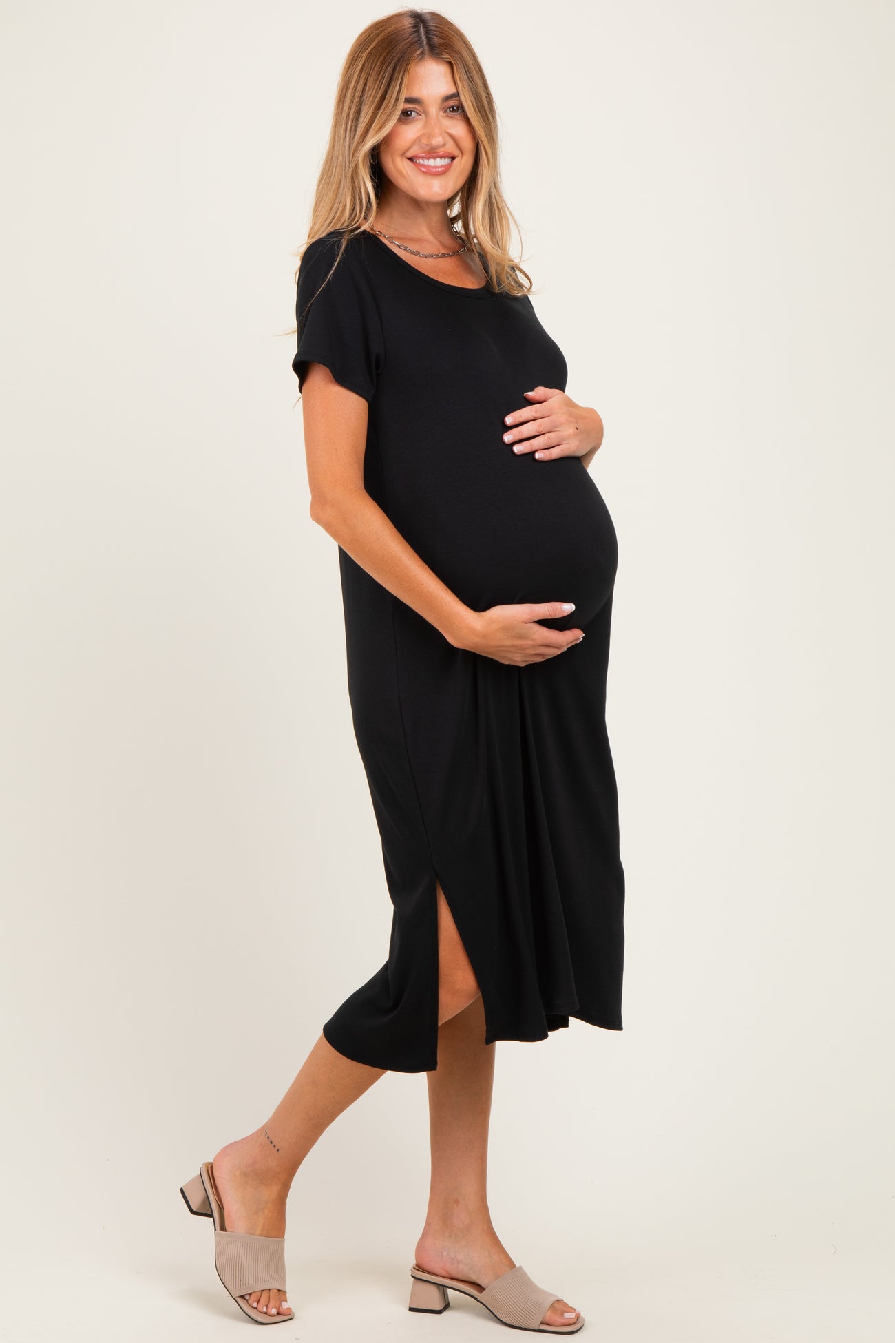 woman wearing a black maternity dress with short sleeves and a side slit, holding her baby bump