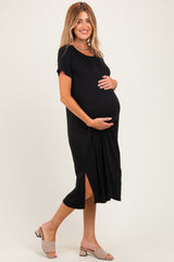 woman wearing a black maternity dress with short sleeves and a side slit, holding her baby bump
