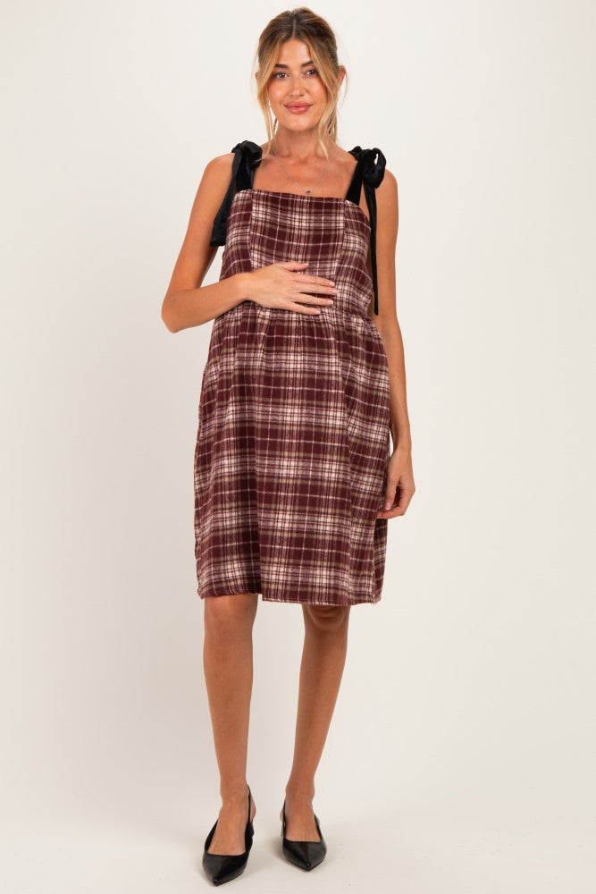 woman wearing a burgundy checkered maternity dress with black bow straps and a visible baby bump