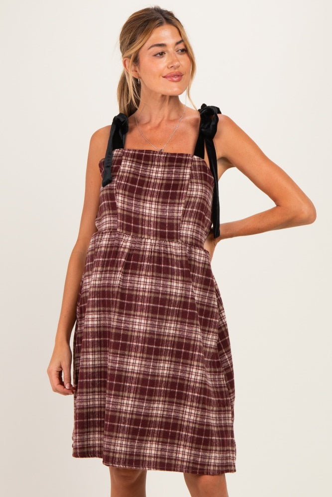 woman wearing a burgundy plaid maternity dress with black ribbon straps and a cinched waist