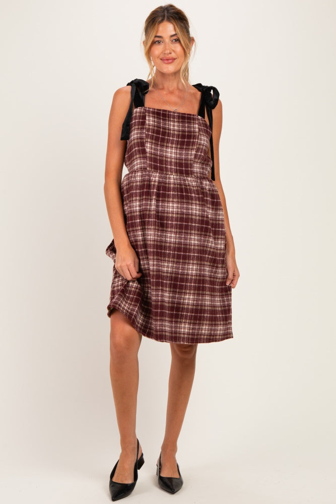 woman wearing a burgundy plaid maternity dress with black satin shoulder ties and a flared skirt