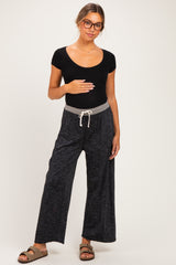 woman wearing a black ribbed maternity top and gray wide-leg maternity pants, holding her baby bump