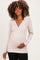 woman wearing a light pink maternity long sleeve top, gently cradling her baby bump