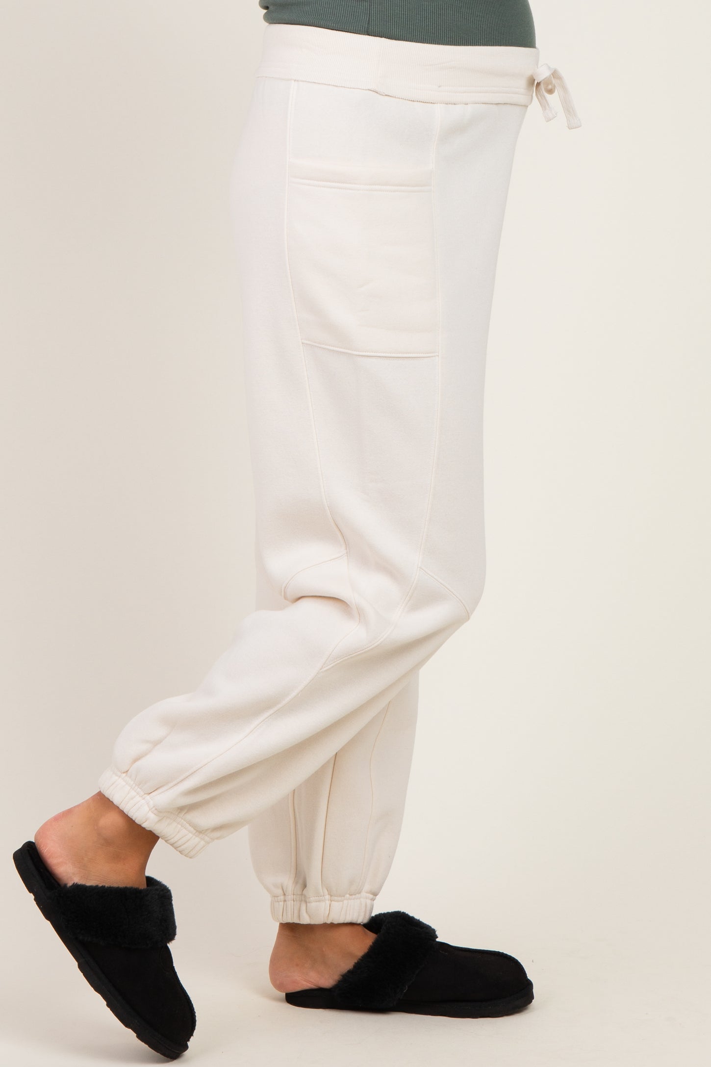 woman wearing white maternity jogger pants with pockets and adjustable waist, paired with black fuzzy slippers