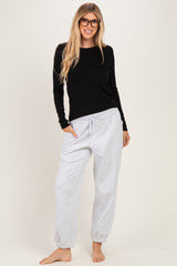 woman wearing a black long sleeve top and light grey drawstring jogger pants, smiling and standing barefoot