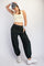 woman wearing a light yellow crop top and dark green sweatpants with pockets, styled with a cap and white sneakers