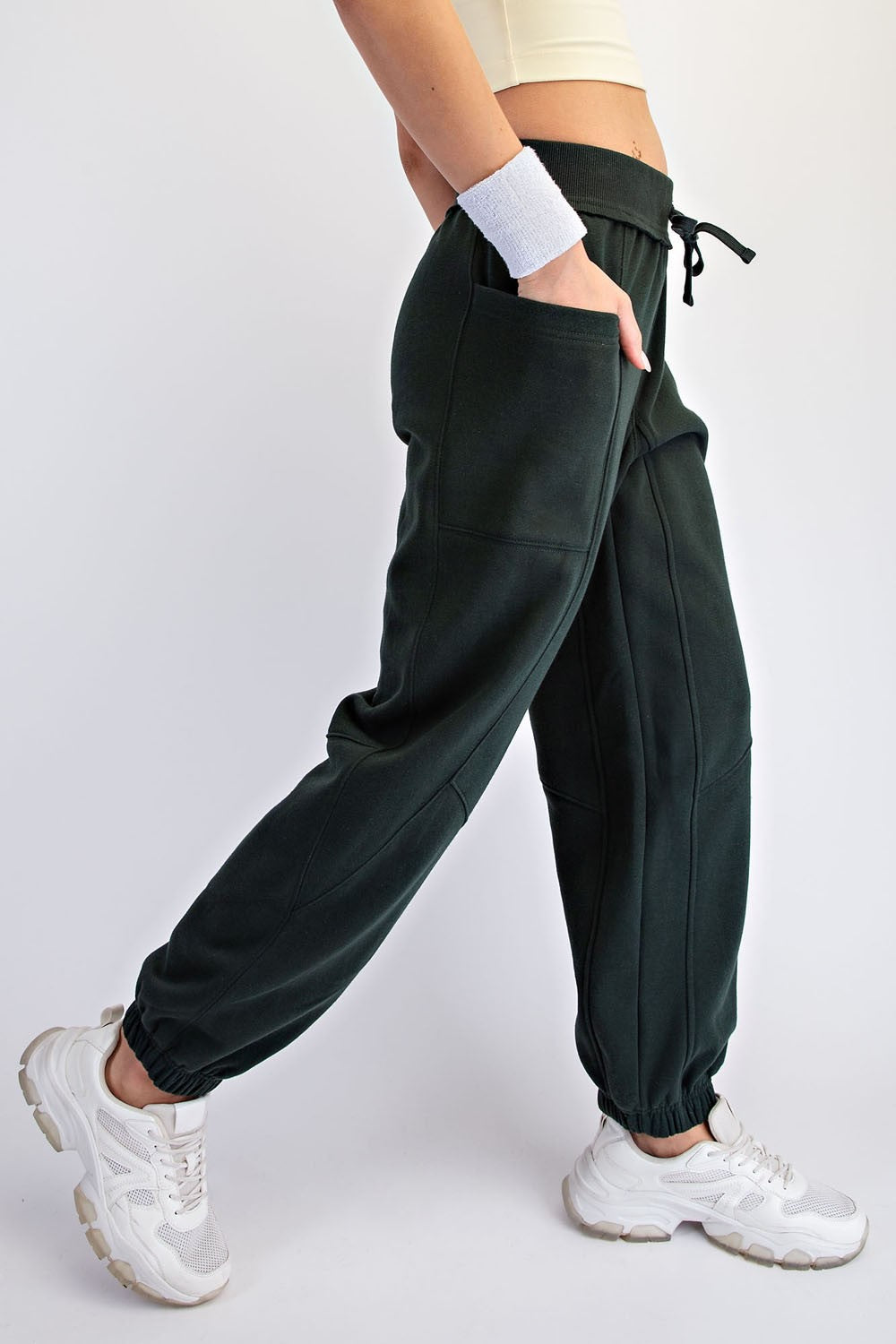 woman wearing dark green jogger pants with side pockets and elastic cuffs, styled with a cropped top and white sneakers