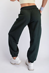 woman wearing dark green sweatpants with elastic cuffs and pockets, styled with a beige crop top and white sneakers