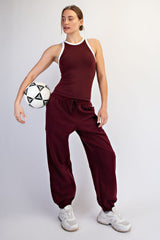 woman wearing a burgundy athletic tank top and matching jogger pants, holding a soccer ball