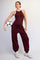 woman wearing a burgundy athletic tank top and matching jogger pants, holding a soccer ball