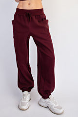 woman wearing burgundy jogger pants with pockets and cuffed ankles, styled with white sneakers