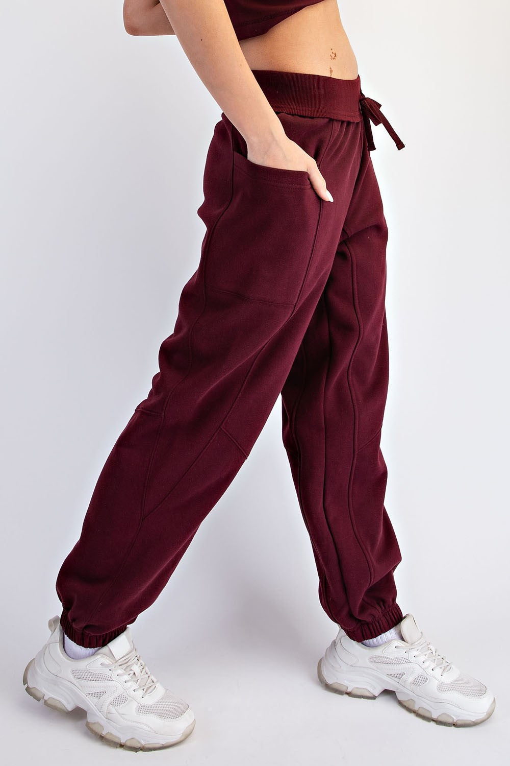 woman wearing burgundy jogger pants with pockets and a drawstring waist, paired with white sneakers