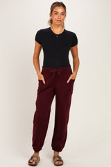 woman wearing a black short sleeve maternity top and burgundy maternity jogger pants with side pockets