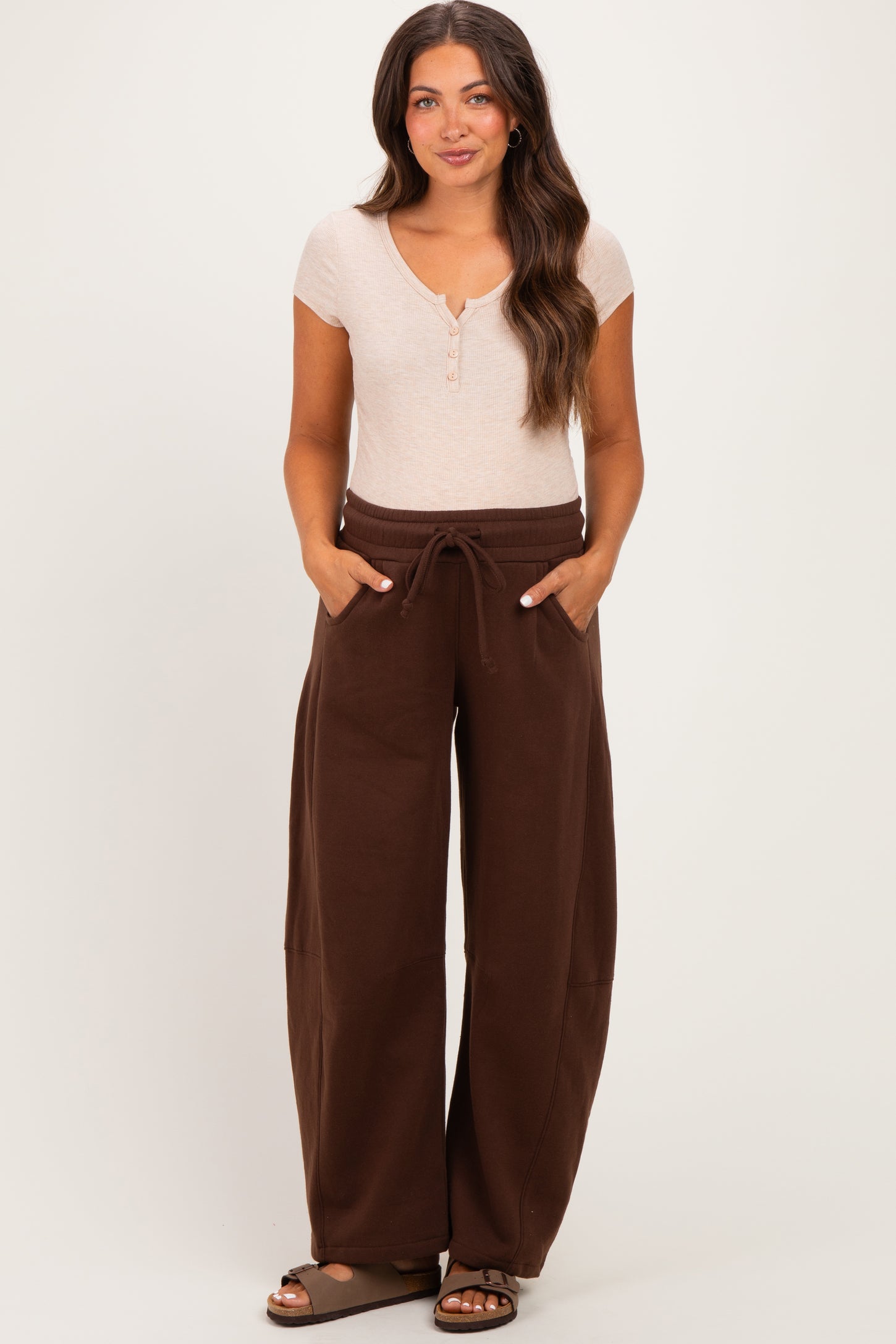 woman wearing a light brown short sleeve henley top and dark brown wide-leg maternity sweatpants with pockets