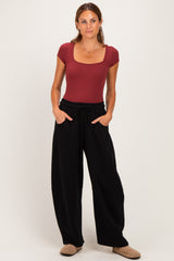 woman wearing a burgundy square neck fitted bodysuit and black wide-leg pants, hands in pockets