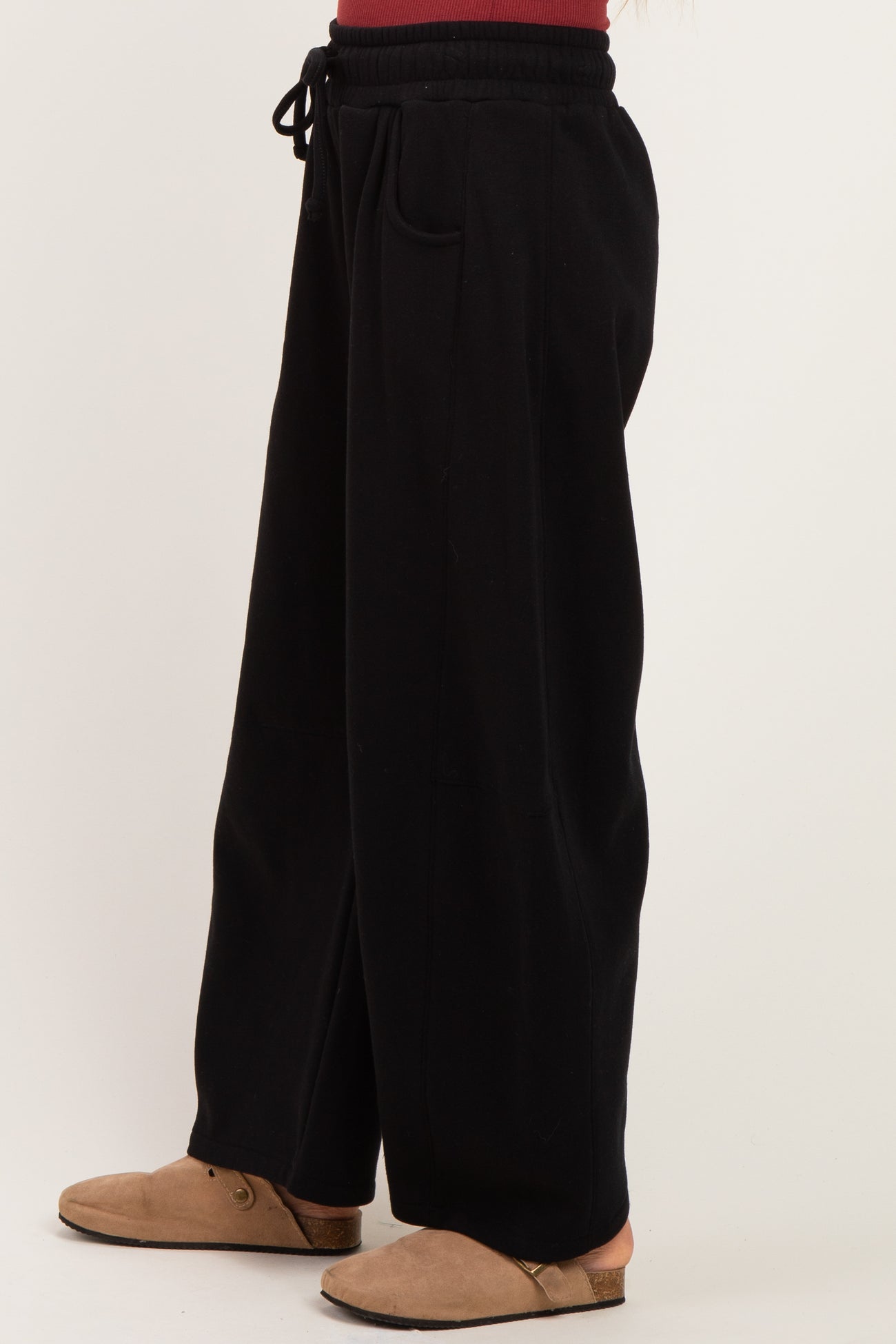 woman wearing black wide-leg sweatpants with an elastic waistband and side pockets, styled with brown slip-on shoes
