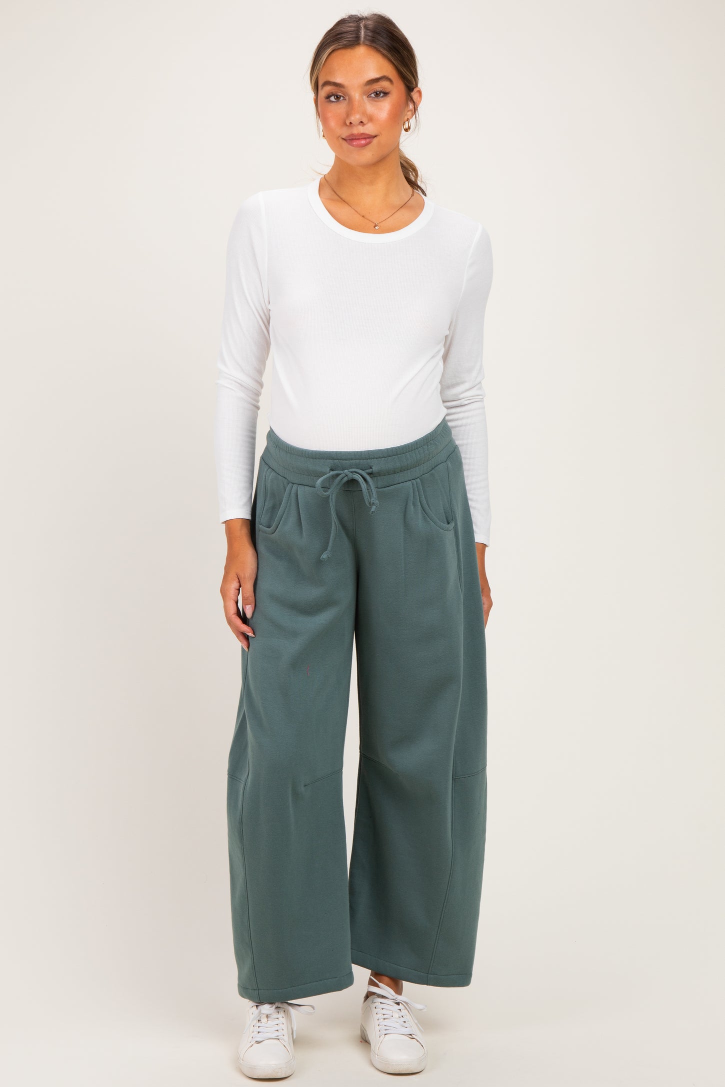 woman wearing a white long sleeve fitted top and green wide leg maternity joggers with an elastic waistband
