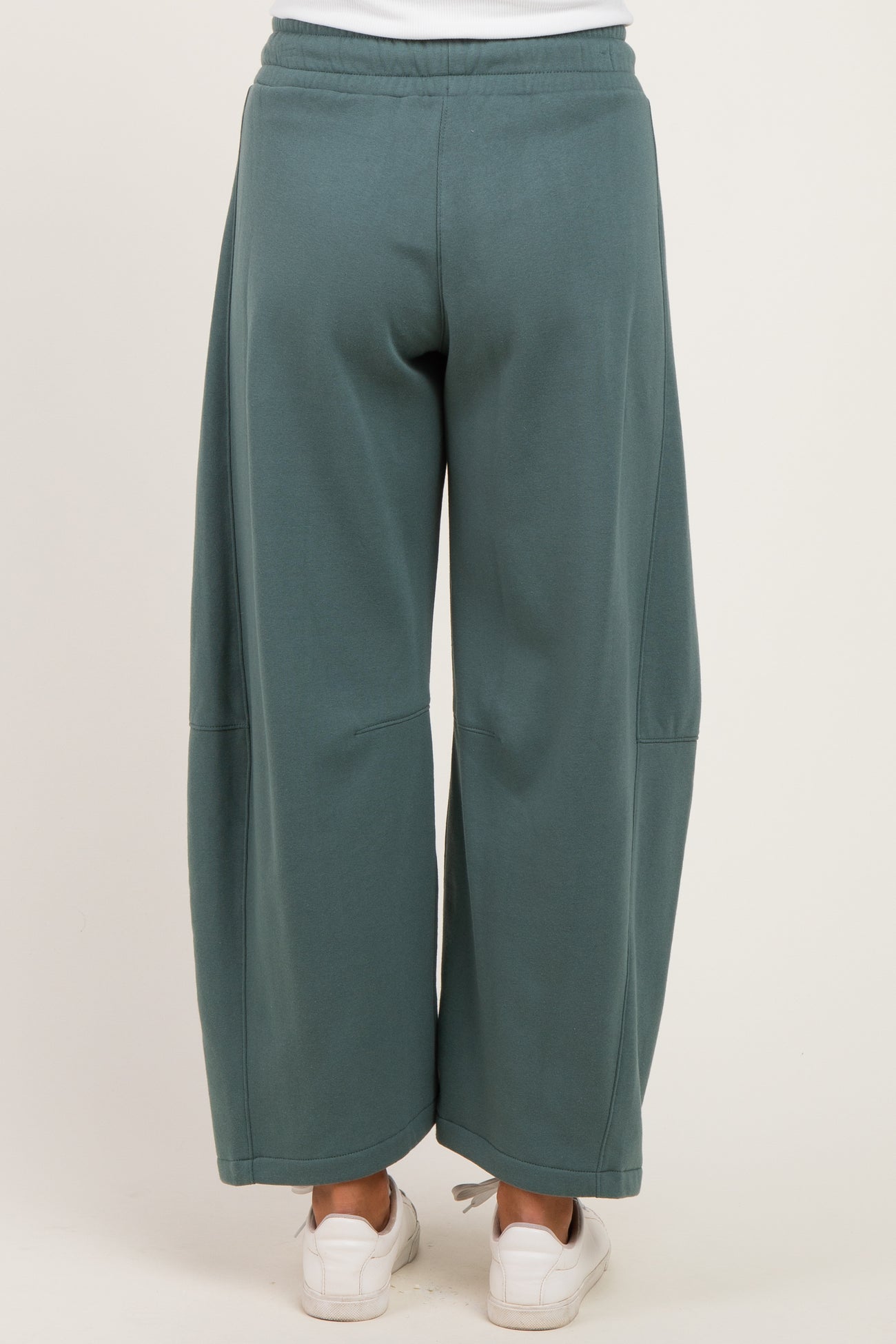 woman wearing a pair of loose-fitting teal maternity jogger pants viewed from the back, paired with white sneakers