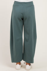 woman wearing a pair of loose-fitting teal maternity jogger pants viewed from the back, paired with white sneakers